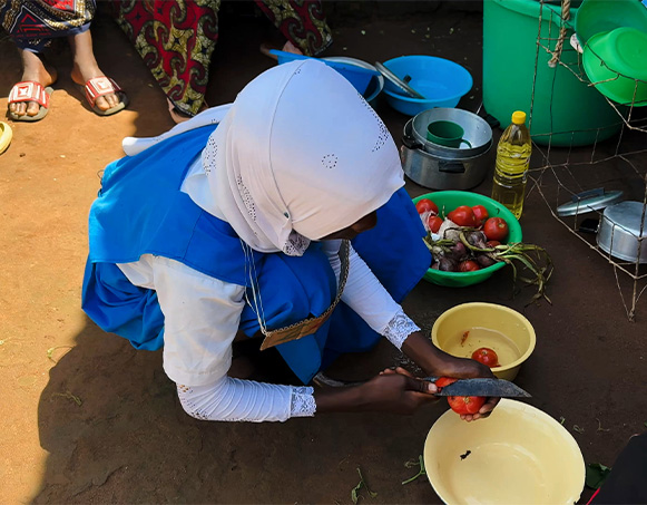 Girl bends over pot, cutting tomato.