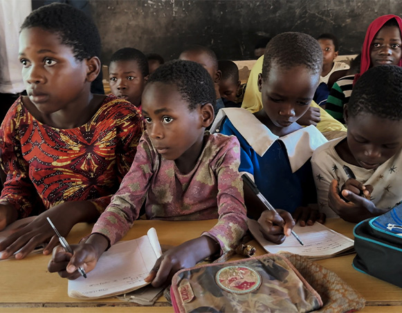 Group of girls crowded around a desk at school, with papers in hand.
